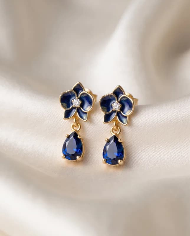 Pendientes Orquídea dorados con una gota facetada azul colgando bajo la flor