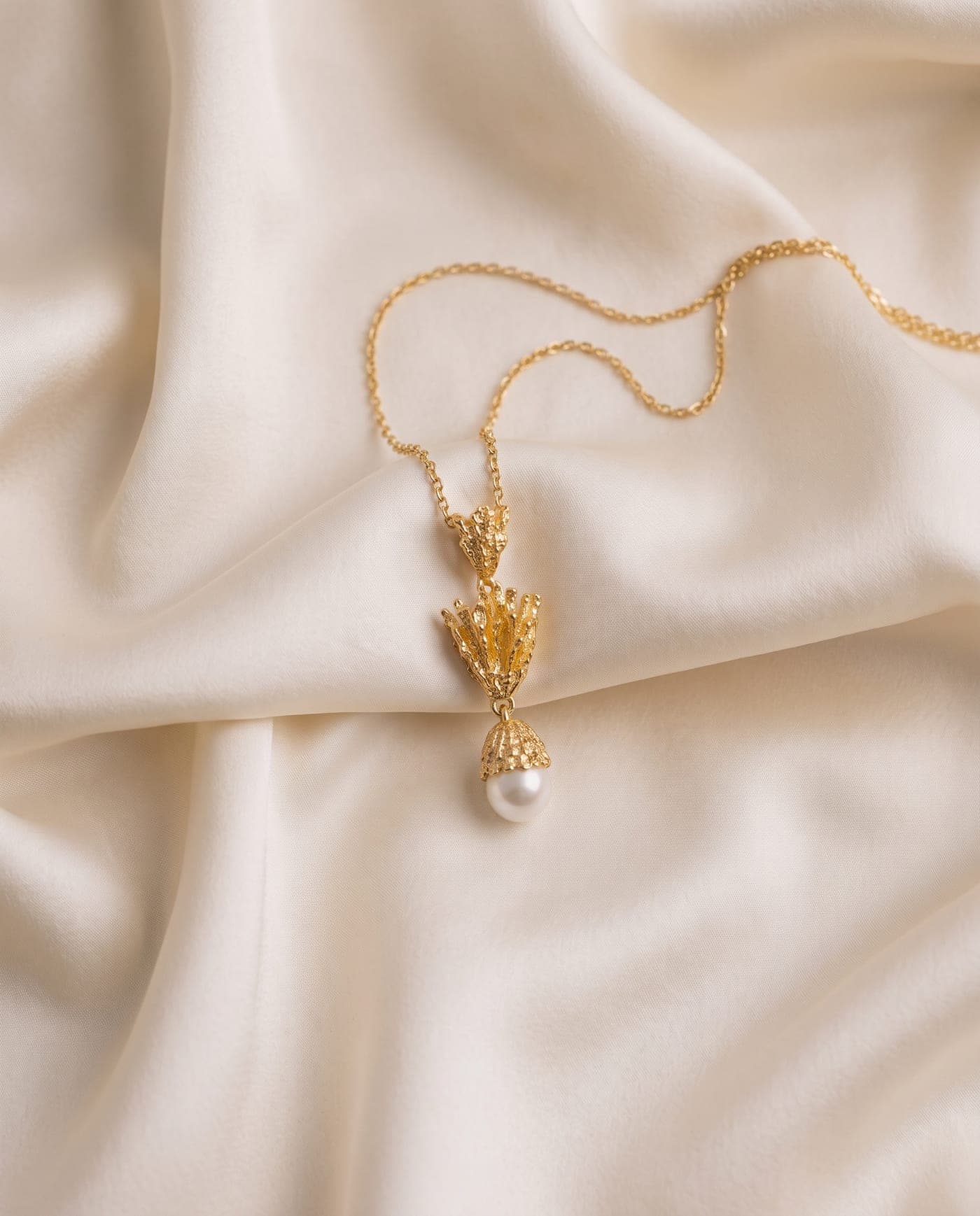 Colección Colección Coral: joya bañada en oro de la línea sobre seda crema, a la luz cálida