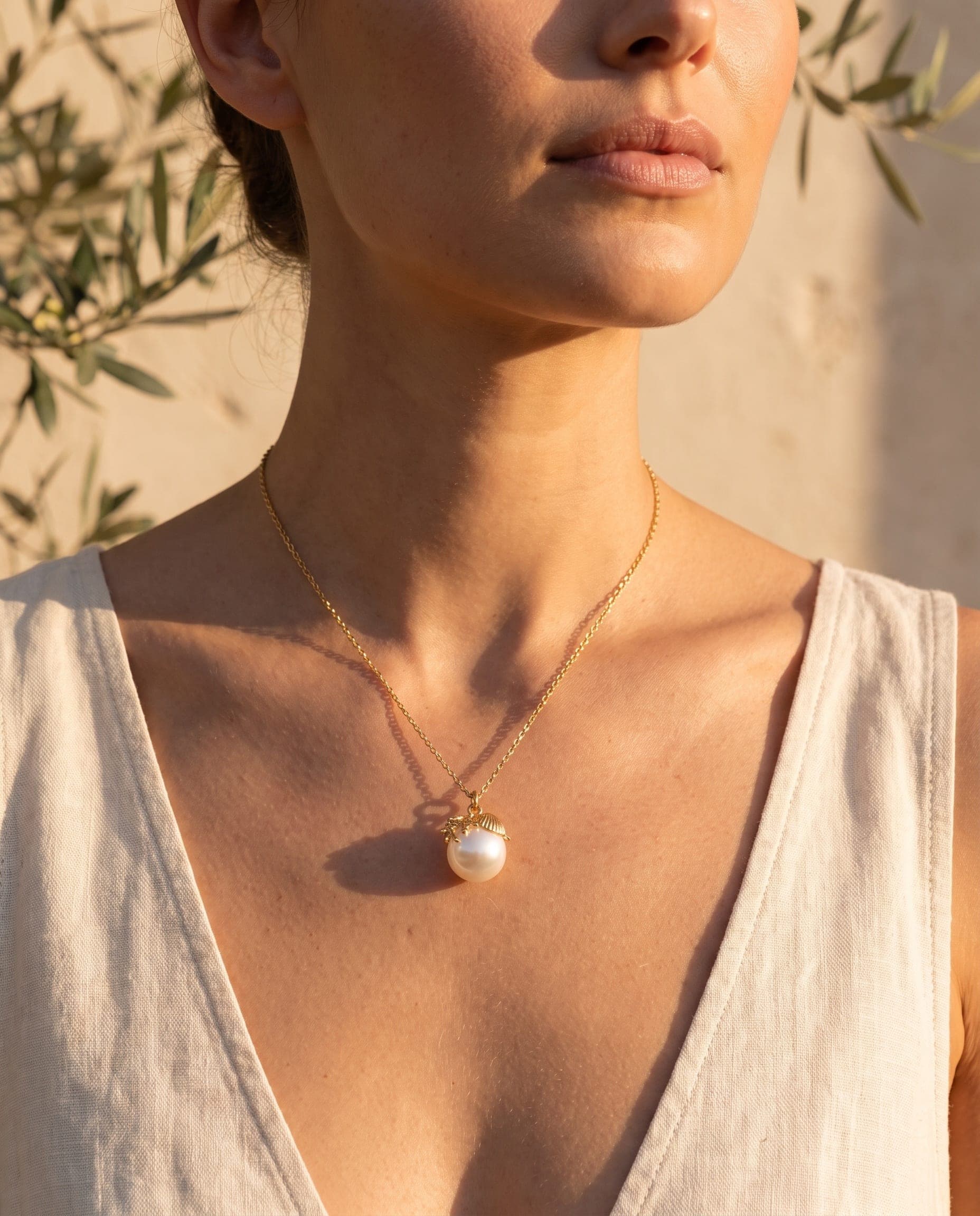 Collar bañado en oro con concha y perla sobre la piel, a la luz cálida de la tarde